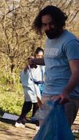 Mann Aktivist mit Zange zu greifen Müll und Plastik Abfall, pflücken oben Müll und Reinigung das Wald Bereich. Freiwillige Sortierung Müll und Recycling Es, konservieren das Natur. Kamera b. video