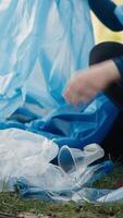 Tired little girl collecting trash and plastic bottles from the forest, helping the volunteers with litter cleanup. Child activist picking up rubbish in a garbage disposal bag. Close up. Camera A. video