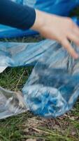 Diverse volunteers collecting trash and storing in the garbage bag, picking up junk and plastic waste to help with forest pollution. Clearing the woods, ecosystem protection. Close up. Camera A. video