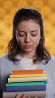 Vertical Portrait of upbeat woman holding pile of books, enjoying reading hobby for entertainment purposes. Radiant bookworm with stack of novels in arms enjoying leisure time, studio background, camera B video