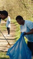 Environmental activists collecting rubbish and plastic waste in garbage bag, using littler cleanup tools to pick up trash from the forest. Women doing voluntary work to protect ecosystem. Camera A. video