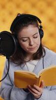 Vertical Lady browsing pages, doing voiceover reading of book to produce audiobook. Voice actor preparing to use storytelling skills to entertain audience while recording novel, studio background, camera B video