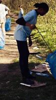 miljö- aktivister samlar skräp och plast avfall i sopor väska, använder sig av mindre städa verktyg till plocka upp skräp från de skog. kvinnor håller på med frivillig arbete till skydda ekosystem. kamera b. video