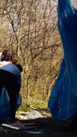 African american girl picking up trash with a long claw and garbage bags, cleaning forest habitat and fighting illegal dumping with a team of volunteers. Activist collecting rubbish. Camera B. video