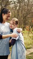 Porträt von Mutter und Tochter Freiwilligenarbeit zu sauber oben ein Wald Bereich, zeigen ein Sinn von Hingabe und Verantwortung zum das natürlich Umgebung Erhaltung. ökologisch Gerechtigkeit. Kamera b. video