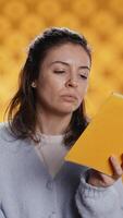 verticaal vrouw lezing boek en genieten van vers appel, leven gezond, geïsoleerd over- studio achtergrond. boekenwurm vermaakt door roman aan het eten groen fruit, genieten van bio tussendoortje, camera b video