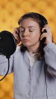 Vertical Woman with headset on starting job, narrating book word for word to produce audiobook. Narrator putting headphones on, using mic to produce digital recording of novel, studio background, camera A video