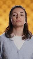 Vertical Portrait of relaxed woman posing, looking at camera, isolated over yellow studio background. Caucasian person dressed in casual attire standing, feeling confident, camera B video