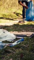 volontär- använder sig av tång verktyg till samla skräp och plast avfall från de skog, lagring skräp i en sopor väska och rena de naturlig miljö. aktivist gripa tag i skräp. stänga upp. kamera b. video