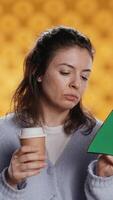 Vertical Woman reading book, turning page and holding disposable cup of coffee, isolated over studio background. Bookworm enjoying novel and caffeinated drink early in the morning, camera B video