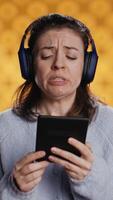 Vertical Voice actor frowns while reading ebook, portraying character, studio background. Woman reenacting digital recording of novel, interpreting furious antagonist, reading text from tablet, camera B video