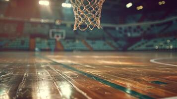 Close-up of a basketball hoop on an empty, well-lit professional court, showcasing the net's intricate details against the soft-focused background of the gleaming wooden floor and the distant seats photo