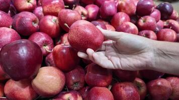 Hand selecting a fresh red apple from a bountiful display at a grocery store, promoting healthy eating and organic produce selection video