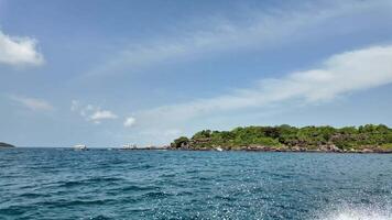 sereno tropicale isola con lussureggiante verde, circondato di blu oceano acque con giro Barche nel il distanza, sotto un' soleggiato cielo con leggero nuvole ideale per vacanza e viaggio concetti video