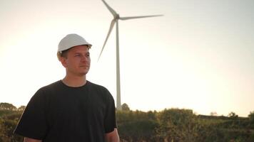 ein Mann im ein schwer Hut Stehen im Vorderseite von ein Wind Turbine draussen video