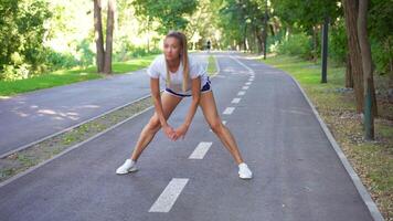 Happy sporty woman jogger doing stretching exercise on road in park video