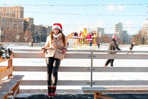Beautiful lovely young adult woman brunet hair warm winter jackets stands near ice skate rink background Town Square. Christmas mood lifestyle photo