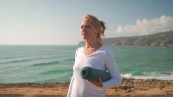 Happy mature woman with rolled yoga mat smiling at beach video