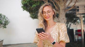 retrato de sonriente mujer en los anteojos utilizando teléfono inteligente en ciudad video