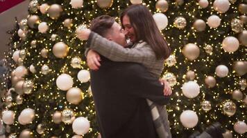 romántico Pareja besos y frotamiento narices cerca Navidad árbol en centro comercial video
