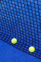 two balls next to a paddle tennis court net, racket sports concept photo