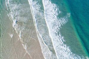olas de un turquesa mar en el apuntalar de un playa, aéreo parte superior zumbido ver foto