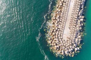 Drone top view of a breakwater with large boulders jutting into the sea. Surrounded by a calm sea. Ideal for backgrounds or travel concepts photo