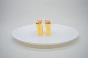 dos rebanadas de queso pastel en un blanco plato con un llanura antecedentes foto