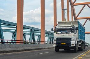 un isuzu gigas tugurio camión pasa terminado un hormigón arco puente, Indonesia, dieciséis enero 2024. foto