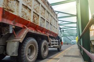 An Isuzu Giga dump truck passes a long steel truss bridge photo