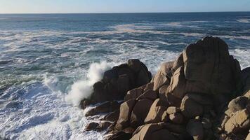rasande hav i de morgon- på gryning vågor rulla på de klippig Strand spray svävar in i de himmel video
