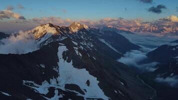 aéreo ver de un Nevado montaña rango con nubes a puesta de sol video