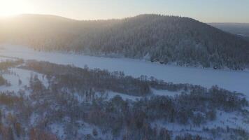 een besneeuwd landschap met bevroren water, bomen, en bergen bekeken van bovenstaand video