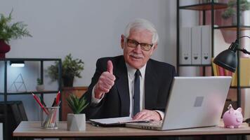 senior bedrijf Mens verhoogt duimen omhoog, is het ermee eens, goedkeuren, houdt mooi zo nieuws gebruik makend van laptop Bij huis kantoor video