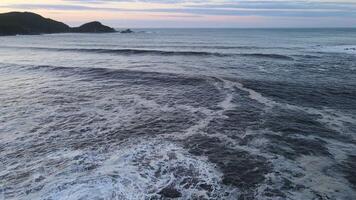 rasande hav i de morgon- på gryning vågor rulla på de klippig Strand spray svävar in i de himmel video