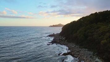 Aerial view of a cliff above ocean, with sunset casting colors on water and sky video