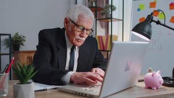 Senior businessman celebrating lonely birthday in office, blowing candle on small cake making a wish video