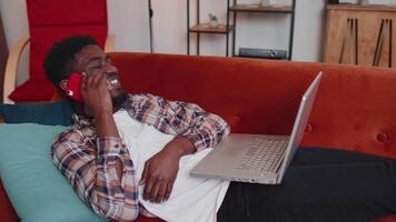 Young man using laptop computer sitting on sofa working, online shopping from home office video