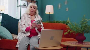 glad nöjd äldre mormor frilansare kvinna brådskande knapp på bärbar dator och räkning pengar video