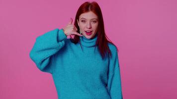 Cheerful girl in blue sweater looking at camera doing phone gesture like says hey you call me back video