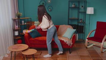 Happy young woman dusting furniture caring for hygiene using colorful duster in living room at home video