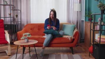 Woman sitting at home using credit bank card and smartphone while transferring money online shopping video