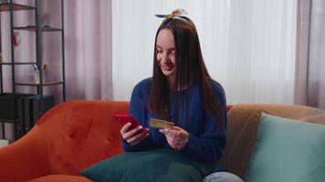 mulher sentado às casa usando crédito banco cartão e Smartphone enquanto transferindo dinheiro conectados compras video