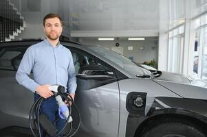 concepto de comprando eléctrico vehículo. hermoso negocio hombre soportes cerca eléctrico coche a concesión foto