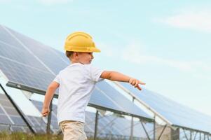 A happy little boy in a yellow helmet is standing on a solar panel farm. photo