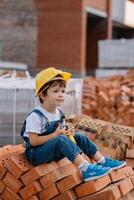 arquitecto en casco escritura alguna cosa cerca nuevo edificio. pequeño linda chico en el edificio como un arquitecto foto