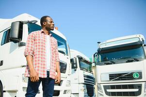 negro hombre camión conductor cerca su camión estacionado en un estacionamiento lote a un camión detener. foto
