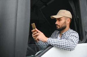 A driver sitting inside the semi-truck while looking through the open window with multiple trucks parked in the background photo