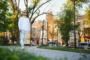 Young handsome blinded man walking with stick in town photo