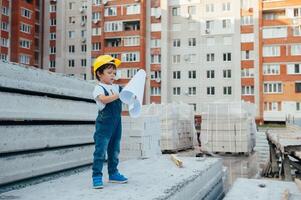 arquitecto en casco escritura alguna cosa cerca nuevo edificio. pequeño linda chico en el edificio como un arquitecto foto